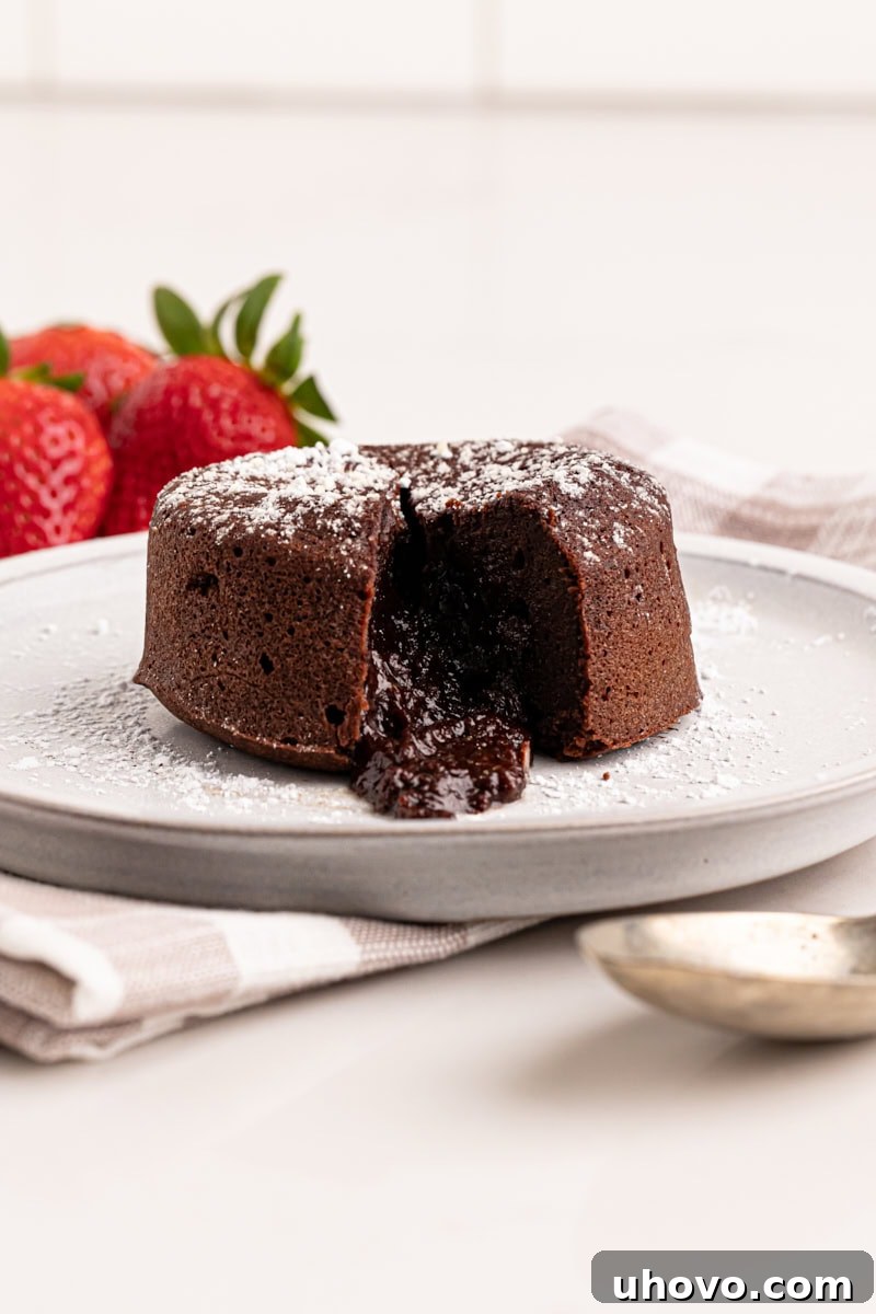 A single chocolate lava cake elegantly presented on a white plate, its dark, glossy exterior promising a rich interior, ready to be cut open.