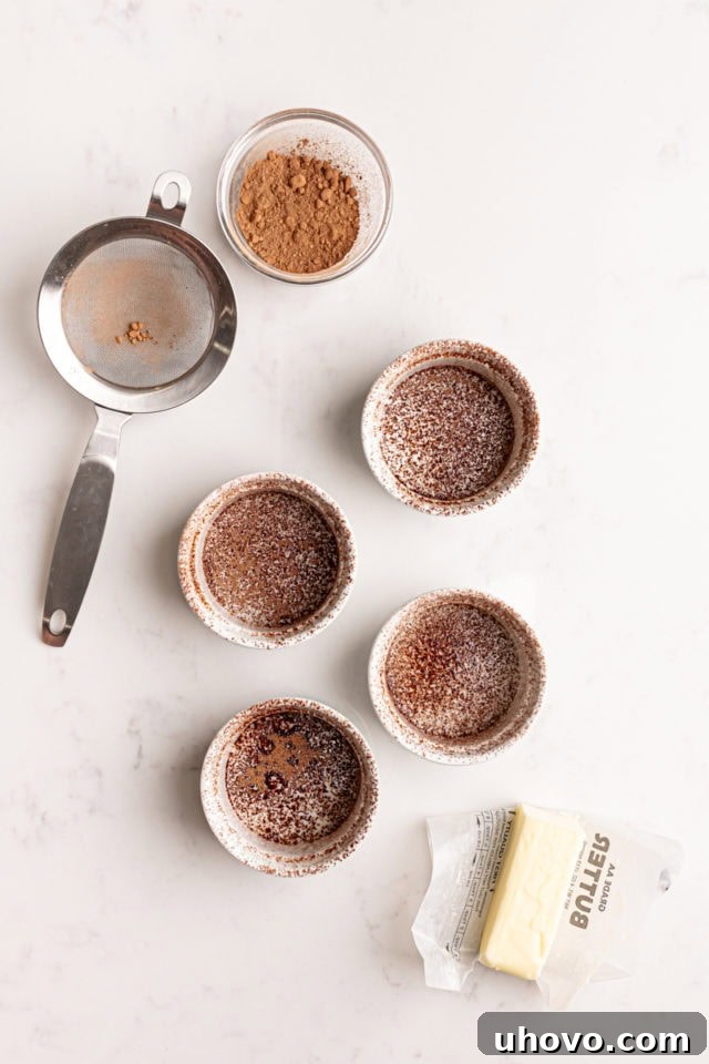 An overhead view of four individual ramekins, meticulously buttered and lightly dusted with cocoa powder, prepared and ready for the lava cake batter.