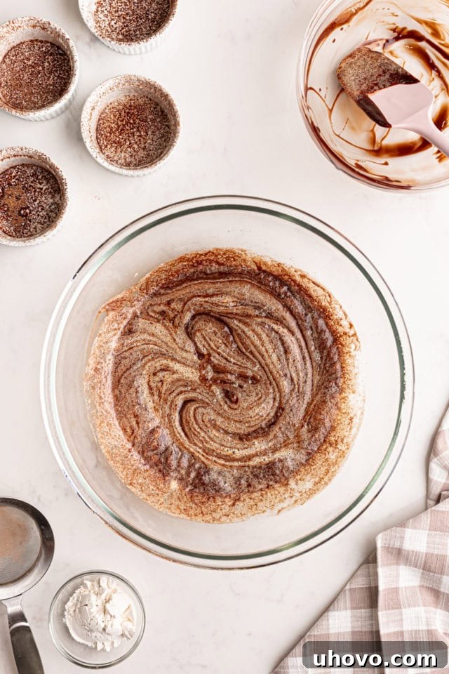 An overhead view of the combined chocolate, butter, eggs, and sugar mixture, showing a spatula gently folding the ingredients together to create a cohesive batter.