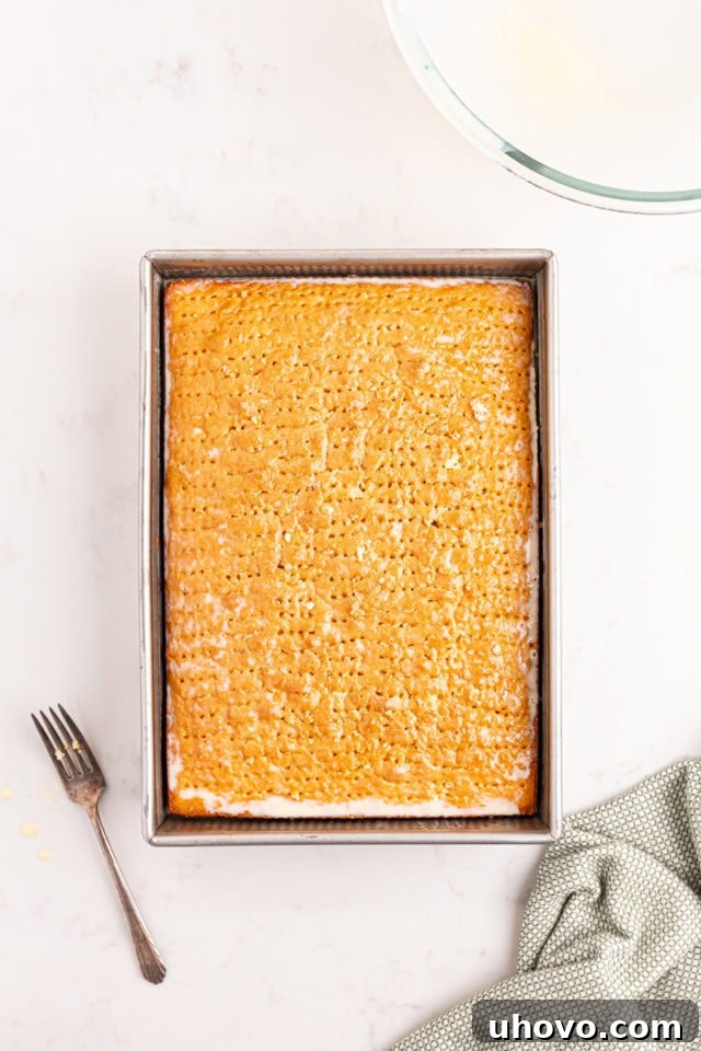 Overhead view of the three-milk mixture being slowly poured over the poked tres leches cake, visibly soaking into the sponge.