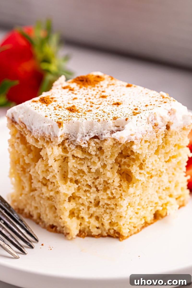A close-up of a slice of tres leches cake on a white plate, with a bite missing, emphasizing its irresistible moistness and delightful texture.