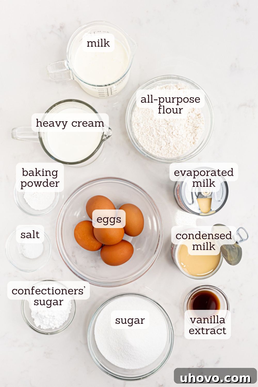 An overhead view of essential ingredients for tres leches cake laid out on a clean surface, ready for preparation.