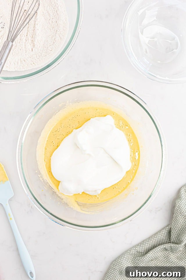 Overhead view of the light and airy whipped egg white mixture being carefully folded into the richer egg yolk mixture.