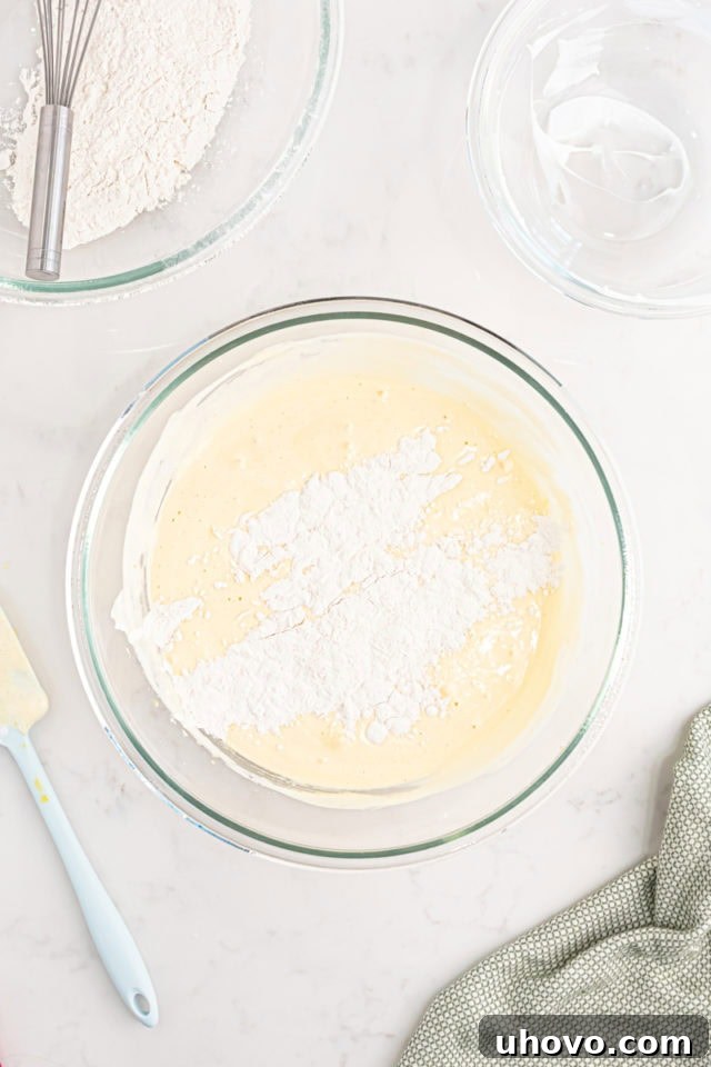 Overhead view of dry ingredients being delicately folded into the wet batter for tres leches cake, ensuring a light and airy consistency.