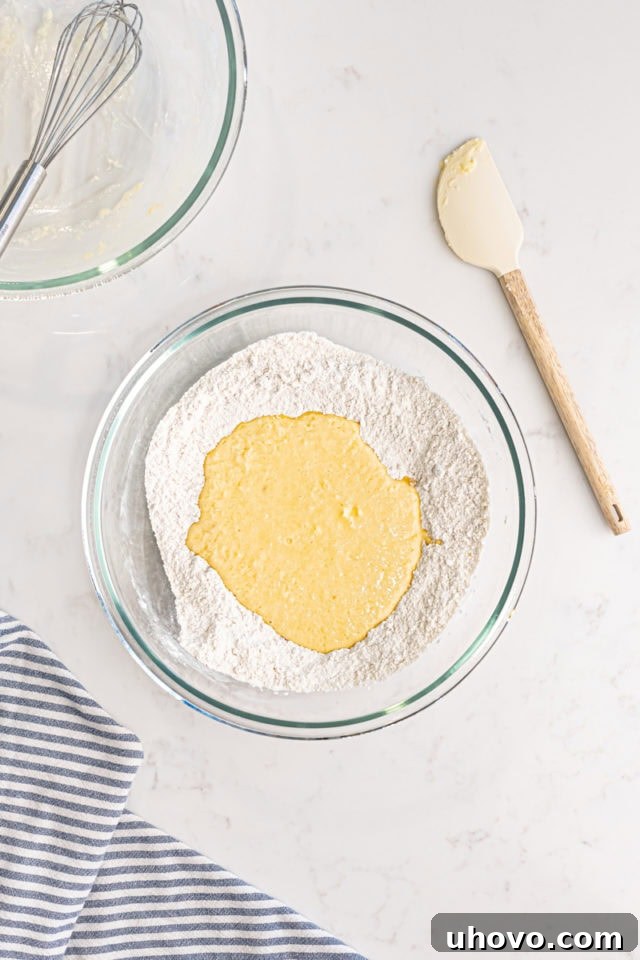 Overhead view of wet ingredients being poured into the bowl of dry ingredients, illustrating the combining step for baked doughnuts.