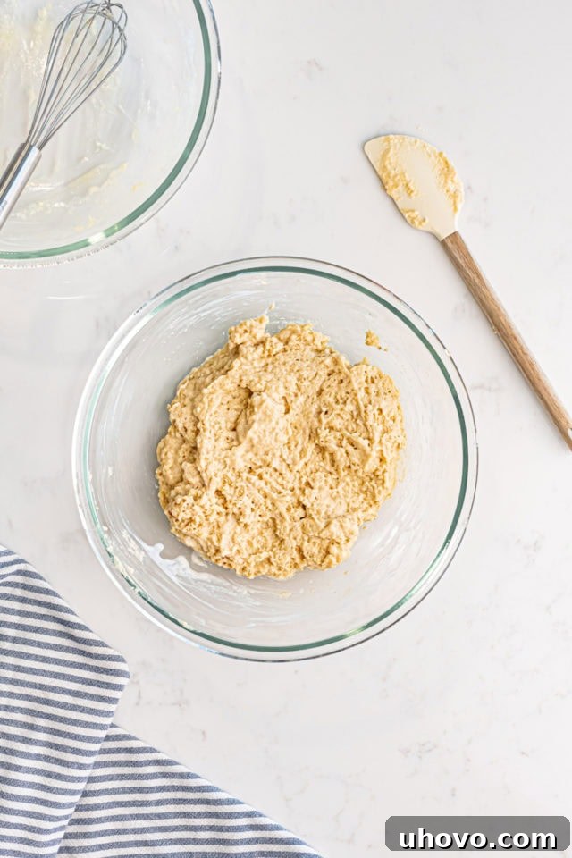 Overhead view of the thoroughly mixed baked doughnuts batter in a glass mixing bowl, showing a smooth but slightly lumpy consistency.