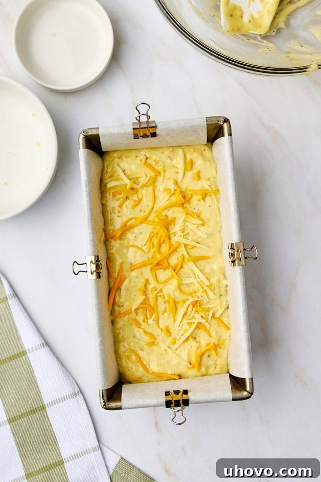 overhead view of shredded cheese sprinkled over the top of herb and cheese quick bread batter in a loaf pan