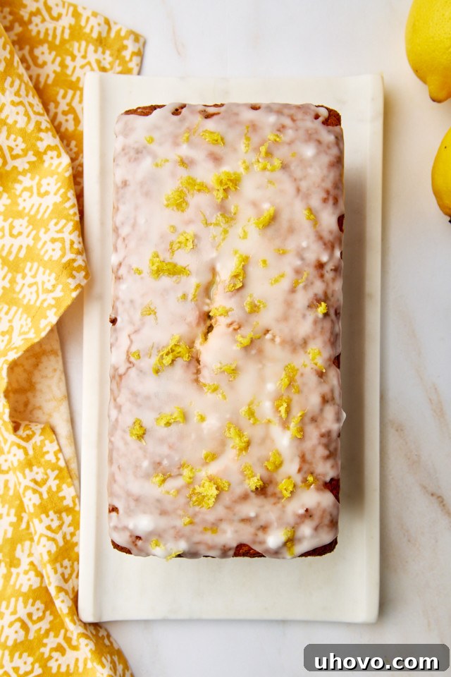 An overhead view of a perfectly glazed lemon poppy seed loaf on a pristine white serving tray, beautifully adorned with extra lemon zest, ready to be served.