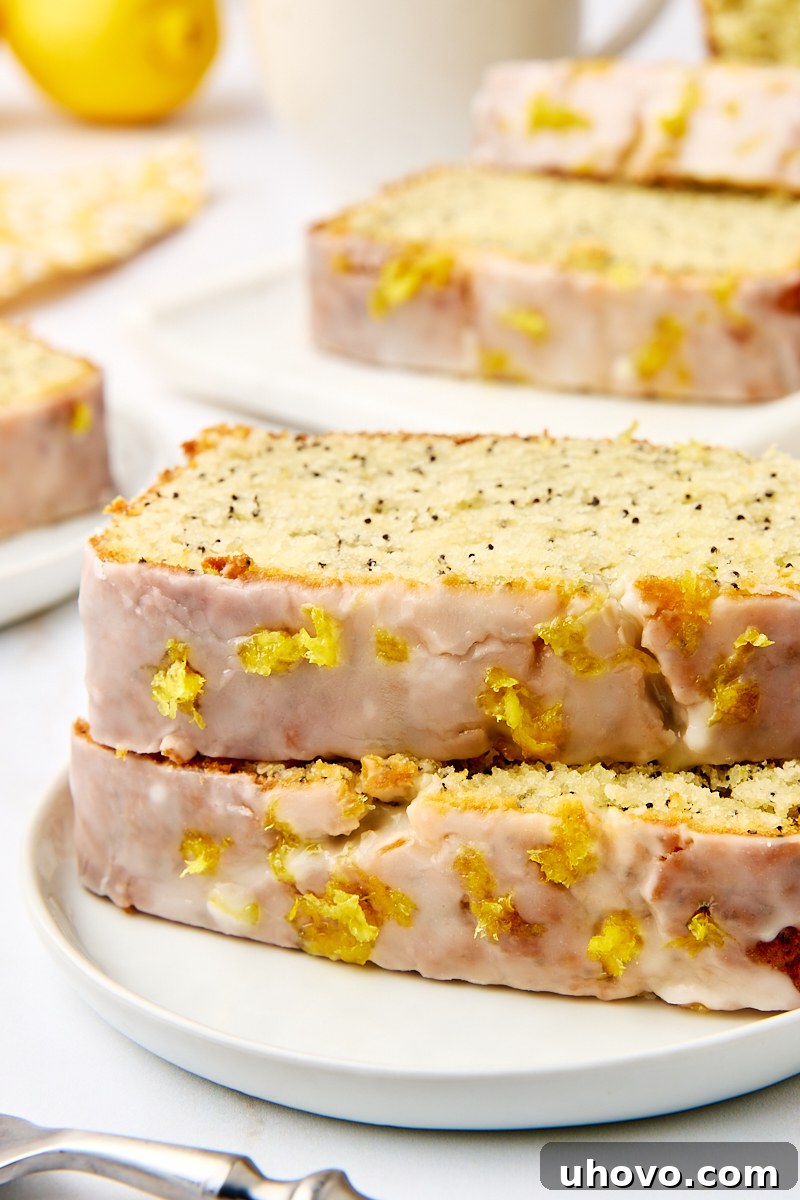 Two perfectly stacked slices of moist lemon poppy seed loaf, revealing the bright yellow crumb speckled with poppy seeds, on a simple white plate.