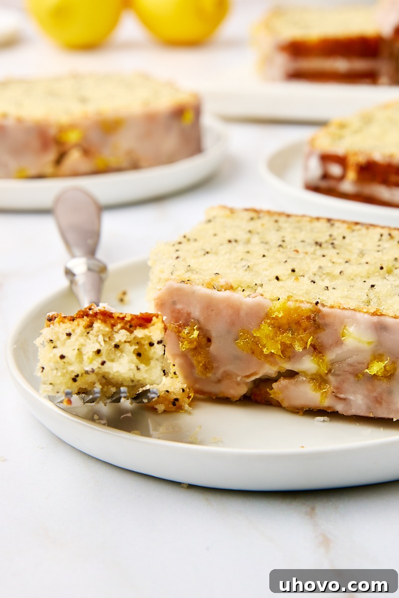 A delightful slice of lemon poppy seed loaf on a white plate, with a fork taking a bite, showing its soft interior.