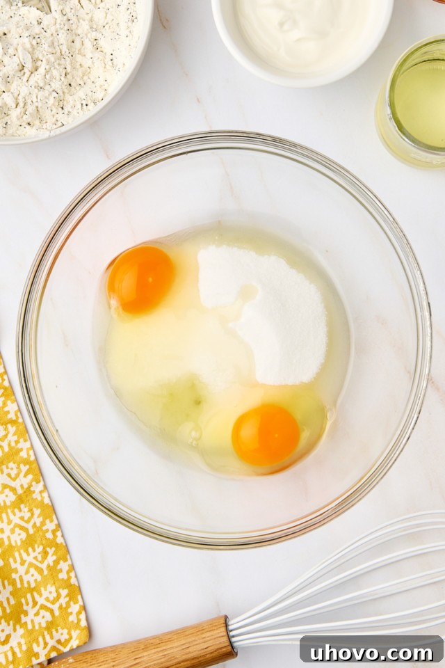 An overhead view of granulated sugar and large eggs perfectly combined in a mixing bowl, being whisked until light and fluffy for the loaf batter.