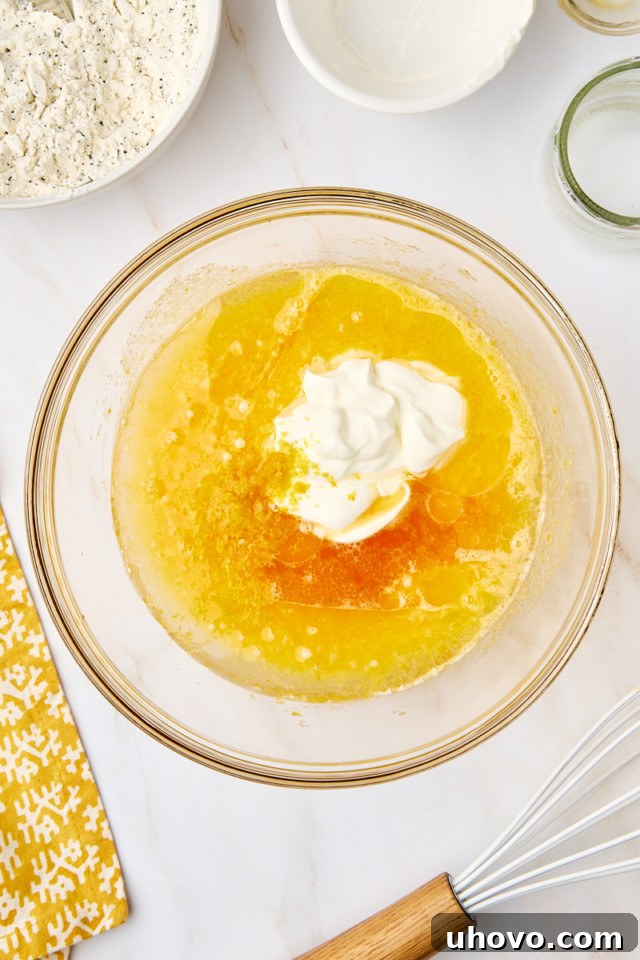 An overhead view of sour cream, vegetable oil, fresh lemon juice, aromatic lemon zest, and a splash of vanilla extract being added to the whisked sugar and egg mixture in a bowl.