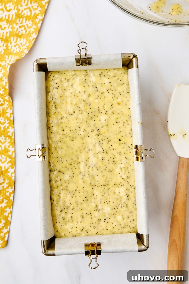 An overhead view of the lemon poppy seed loaf batter smoothly spread into the prepared loaf pan, ready for baking in the oven.
