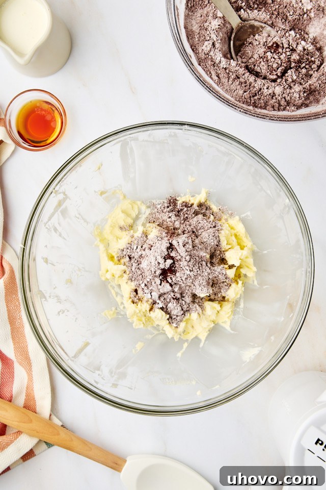 A mixture of sifted confectioners' sugar, cocoa powder, and salt being slowly added to the creamed butter for chocolate frosting.