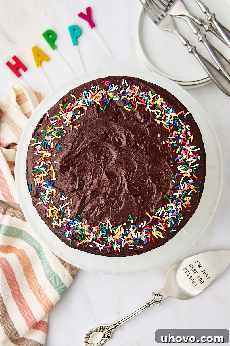An overhead view of a magnificent yellow cake with chocolate frosting, beautifully presented on a white cake plate, surrounded by elegant dinnerware and festive birthday candles.