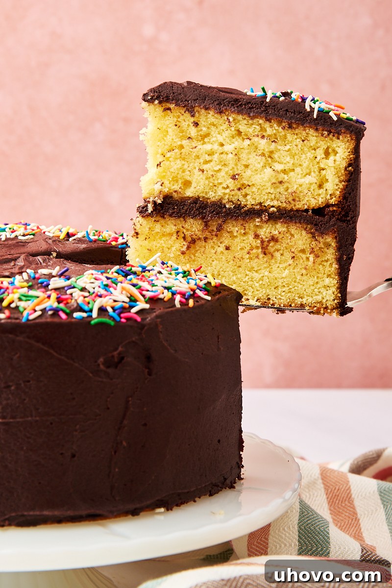 A delectable slice of yellow cake with chocolate frosting being gently lifted from the main cake, showcasing its perfect layers and rich topping.