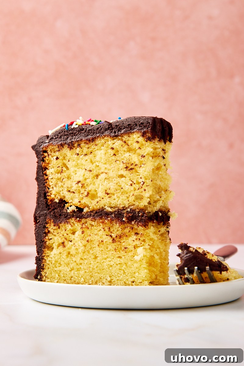 A delicious slice of yellow cake with chocolate frosting on a white plate, with a fork holding a perfect bite, inviting indulgence.