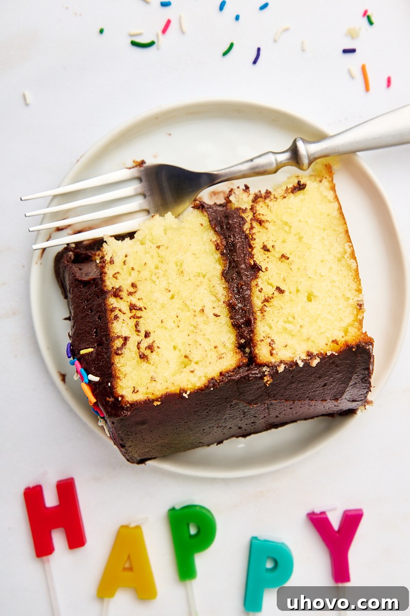 An overhead shot featuring a partially sliced yellow cake with chocolate frosting on a white plate, flanked by whimsical letter-shaped candles spelling out "happy", setting a festive mood.