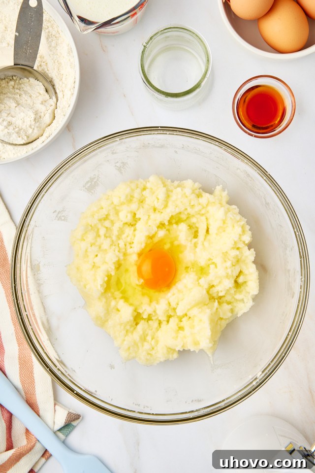 A single egg being added to the creamed butter and sugar mixture in a large mixing bowl, ready to be incorporated.