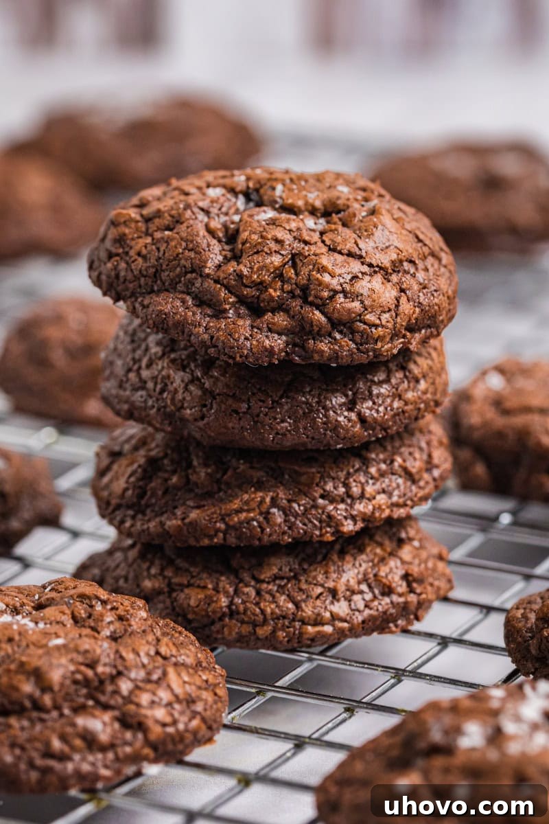 A beautifully stacked tower of four salted chocolate truffle cookies, with more delectable cookies artfully arranged on a wire cooling rack in the background.