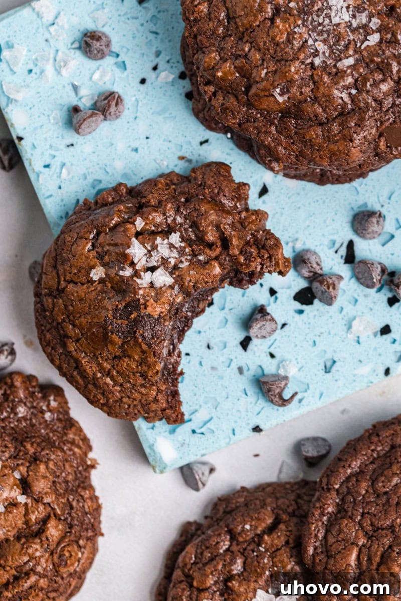 An alluring overhead close-up of a single salted chocolate truffle cookie with a perfect bite taken out, revealing its soft, fudgy interior and crackly top.