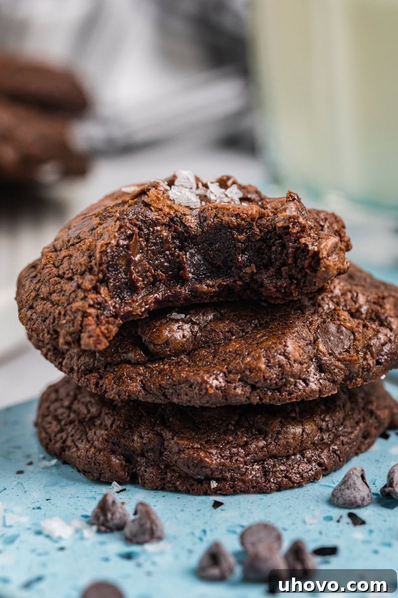 A charming stack of three salted chocolate truffle cookies, with a tempting bite missing from the top cookie, showcasing its soft interior.