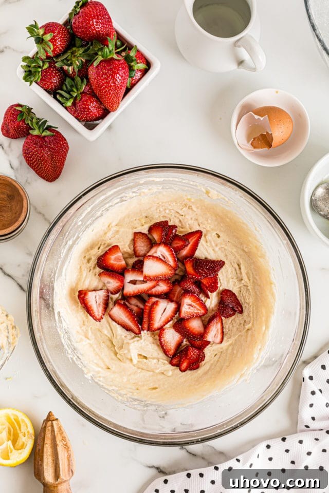 Overhead view of sliced fresh strawberries being gently folded into the cake batter in a bowl, ensuring even distribution.