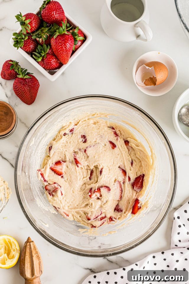 Overhead view of cake batter in a glass mixing bowl after strawberries have been folded in, showcasing the lovely distribution.