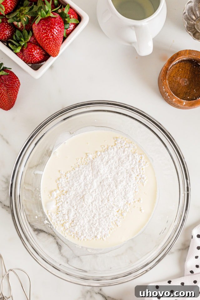 Overhead view of confectioners' sugar and heavy cream in a large glass mixing bowl, ready to be whisked into whipped cream.