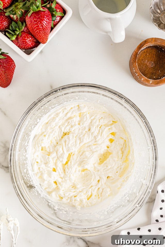 Overhead view of perfectly whipped cream in a glass mixing bowl, showcasing its soft peaks and airy texture.