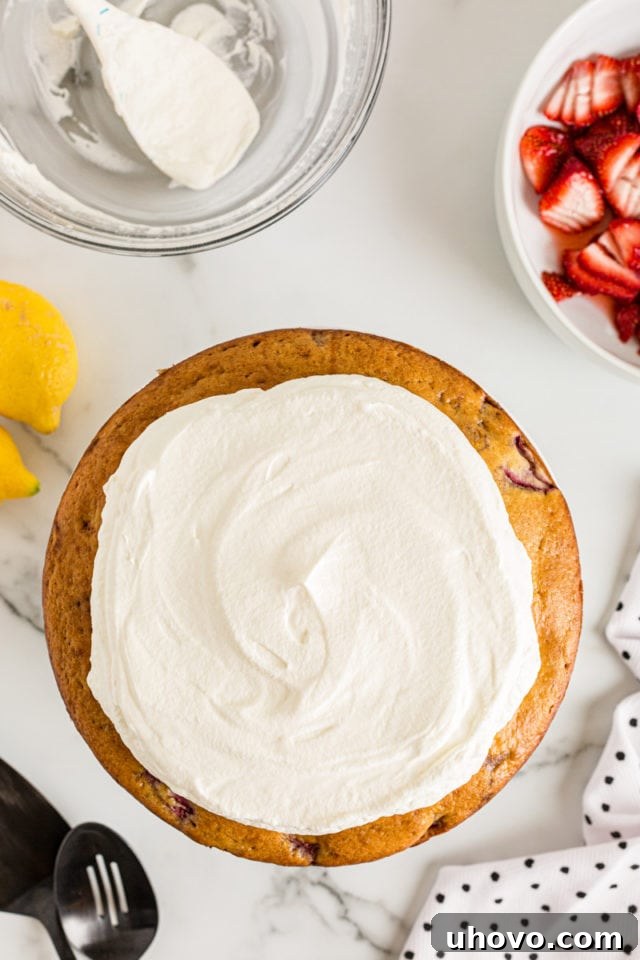 Overhead view of the Lemon-Strawberry Shortcake cake with a generous layer of freshly whipped cream spread on top, before adding strawberries.