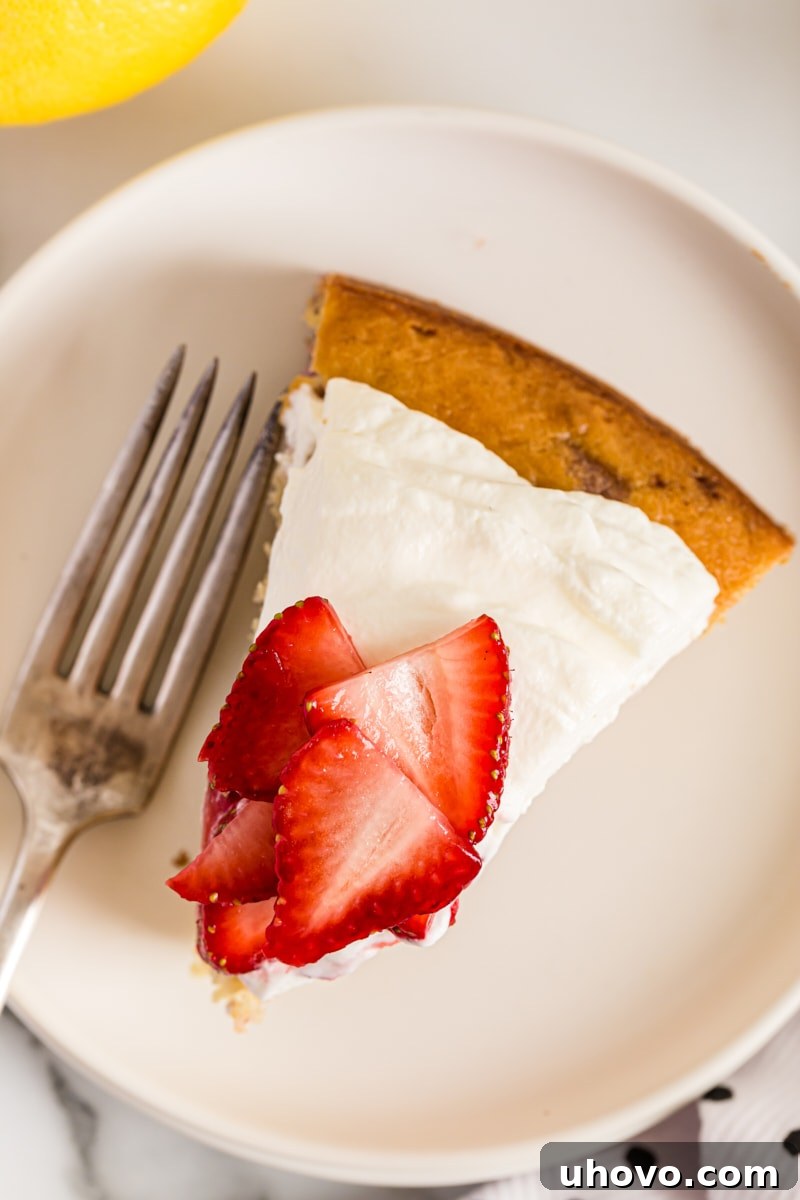 An overhead view of a slice of Lemon-Strawberry Shortcake on a plate with a fork, ready to be enjoyed, showing off its beautiful layers.