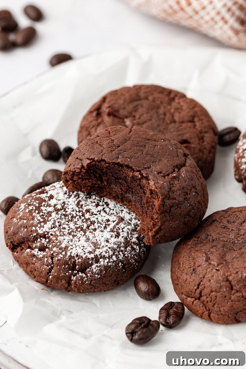 A few chocolate espresso cookies on parchment paper, with one cookie bitten to show fudgy texture