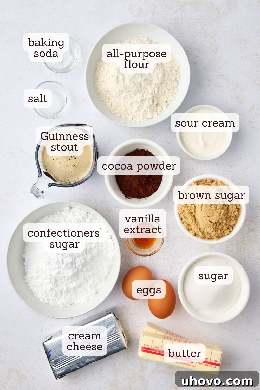 Overhead view of various ingredients for Guinness chocolate cake laid out on a kitchen counter: flour, cocoa, eggs, Guinness, butter, sugars, sour cream.