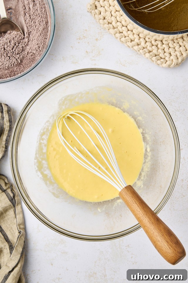 Overhead view of combined eggs, sour cream, and vanilla extract in a glass mixing bowl, whisked smooth.