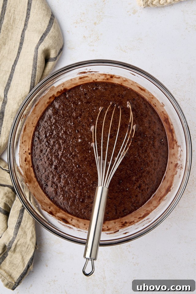 Overhead view of the Guinness chocolate cake batter in a glass mixing bowl, being gently mixed with a whisk.