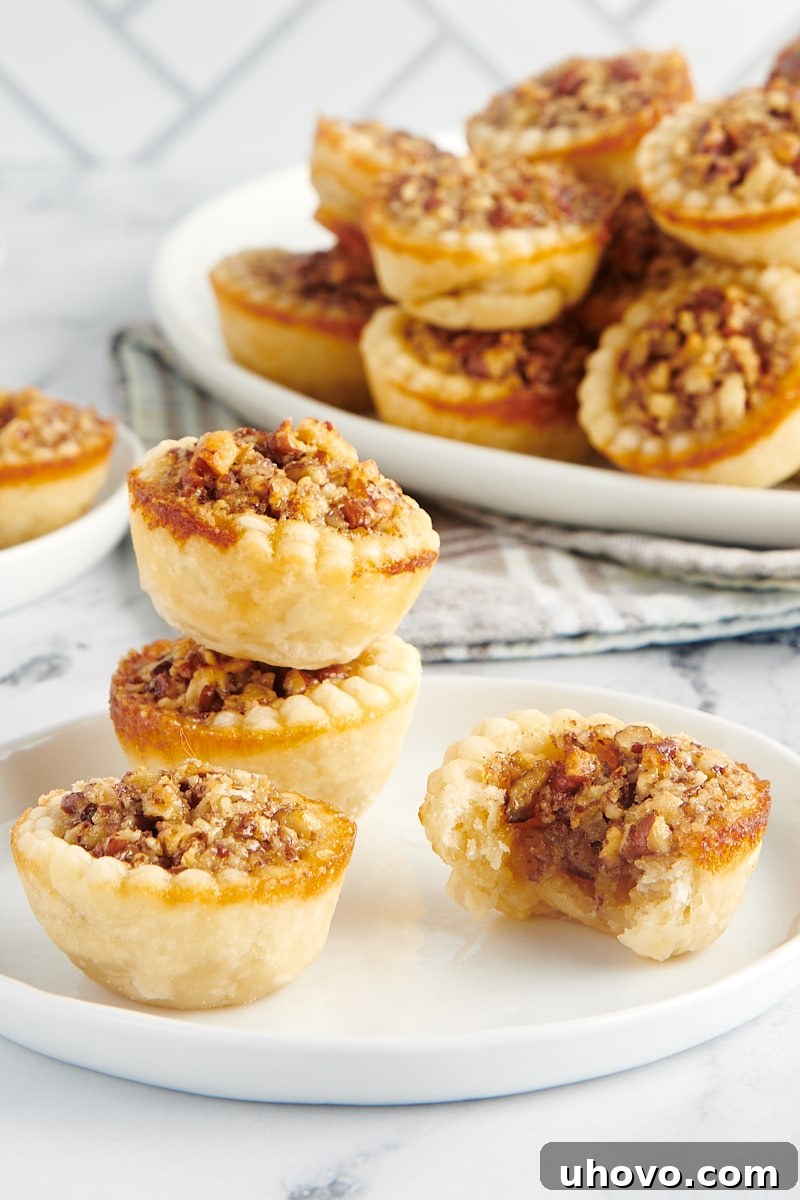 Two mini pecan pies stacked gracefully behind a single whole mini pie and one with a delectable bite taken out, revealing the gooey filling.