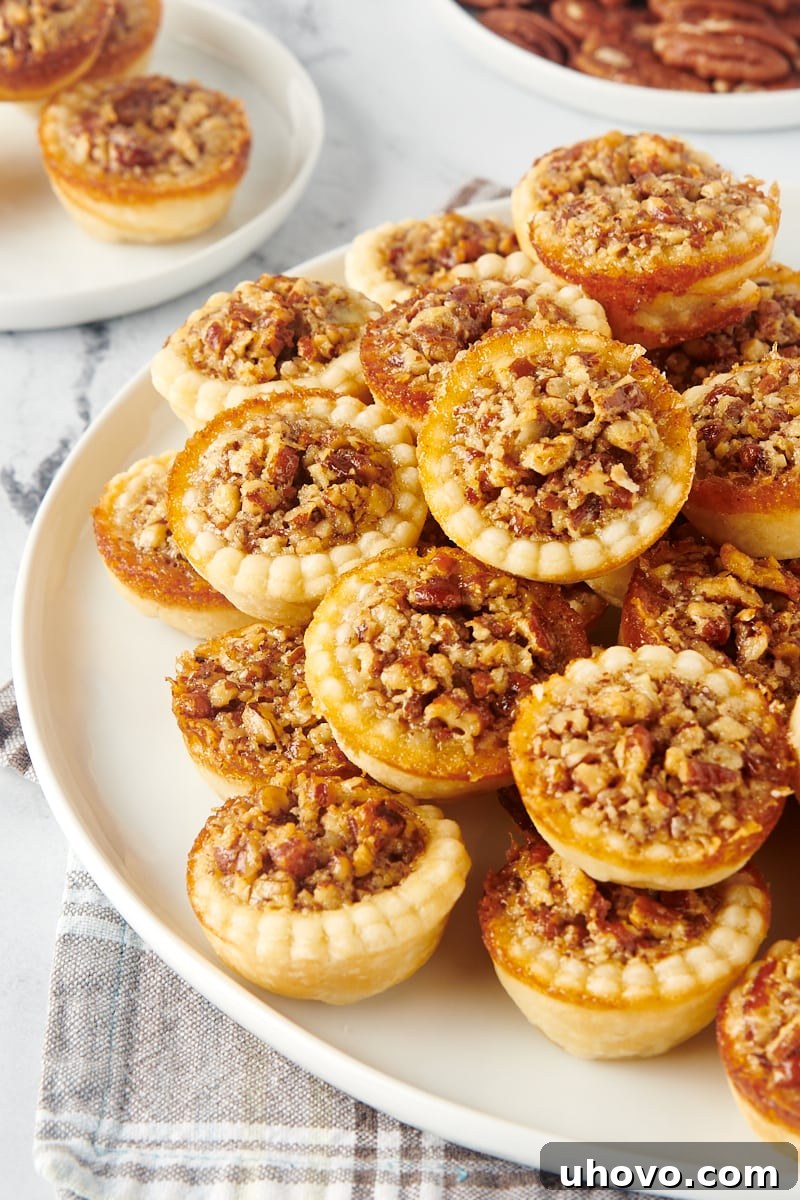 A large platter generously filled with numerous mini pecan pies, with a single plated mini pie in the background, creating an inviting holiday spread.