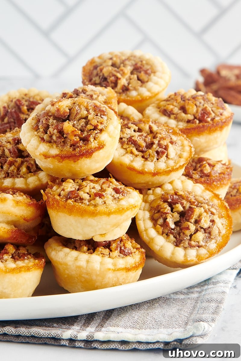 A generous pile of perfectly golden-brown mini pecan pies arranged artfully on a large platter, inviting guests to indulge.