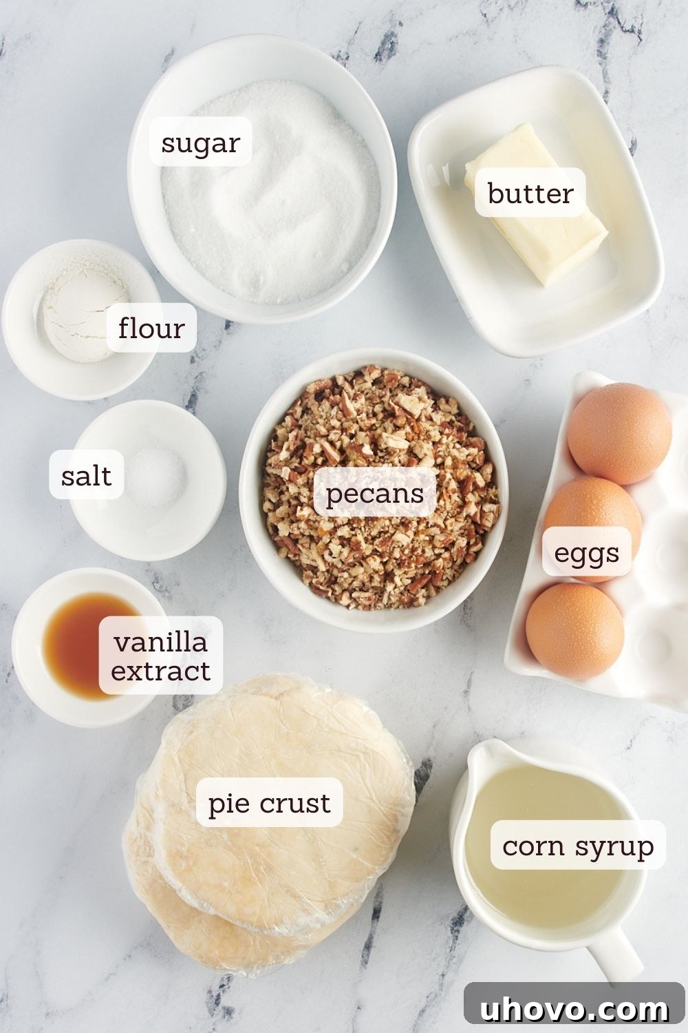 An overhead view of the simple ingredients laid out on a kitchen counter for making mini pecan pies, including pecans, eggs, sugar, butter, and corn syrup.
