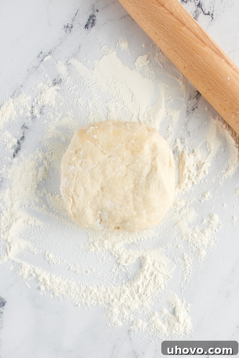 A ball of pie dough rests on a lightly floured countertop, ready to be rolled out, with a rolling pin nearby.
