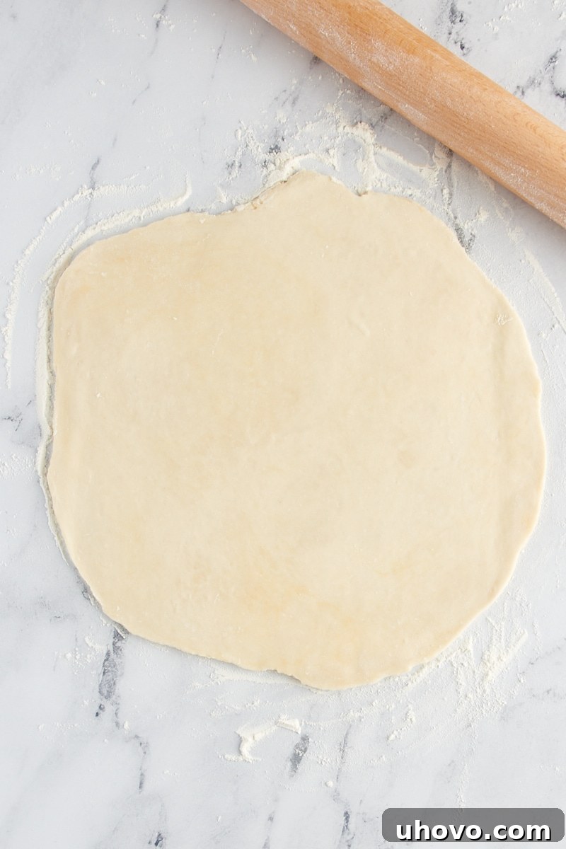 Pie crust meticulously rolled out into a rough circular shape on a flour-dusted countertop, awaiting the next step.