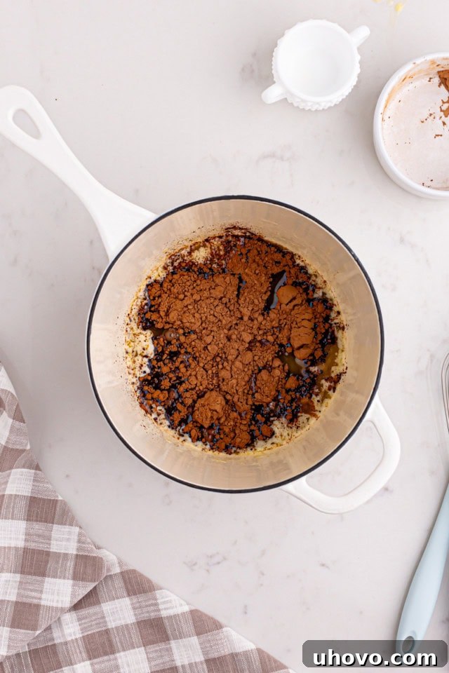 Saucepan on the stove with melted butter, cocoa powder, and milk being whisked together to form the frosting base.