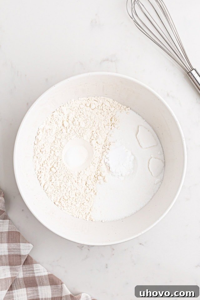 Overhead view of flour, sugar, baking soda, and salt mixed in a white bowl, ready for the wet ingredients.