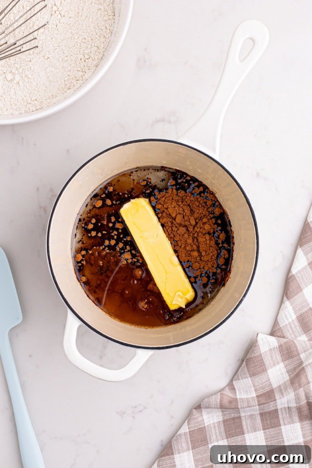 A saucepan on the stove containing butter, vegetable oil, water, and cocoa powder, beginning to melt and combine.