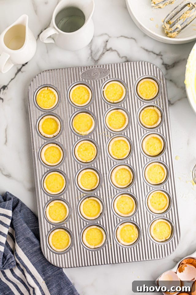 Mini muffin pan filled with Lemon Chess Tartlets, glistening and ready to be placed into the oven for baking.