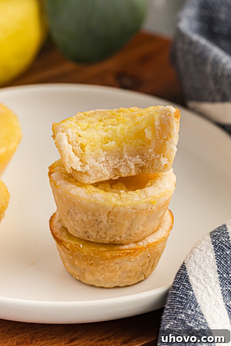 A tempting image of a half Lemon Chess Tartlet perched atop two whole tartlets on a white plate, revealing the creamy lemon filling.