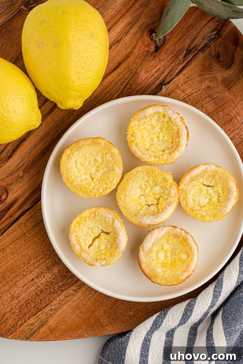 Overhead view showcasing a collection of golden Lemon Chess Tartlets arranged artfully on a white plate, set against a warm wooden surface.