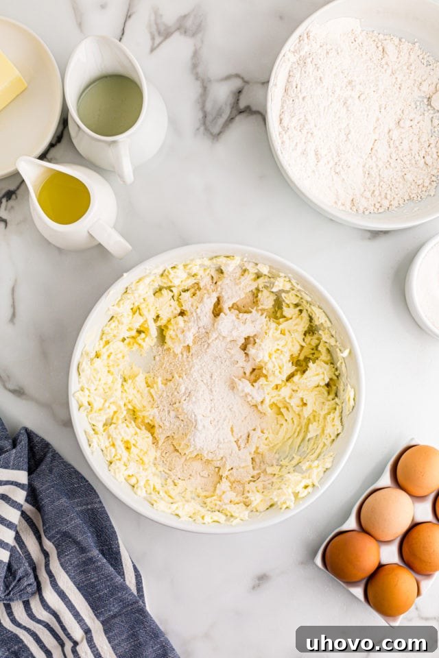 All-purpose flour is gently added to the creamed butter and cream cheese mixture in a white mixing bowl, forming the tartlet crust dough.