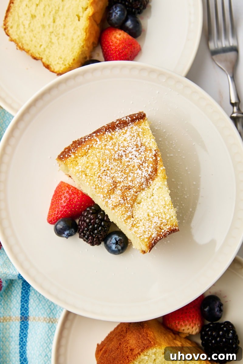 Overhead view of a slice of whipped cream cake on a white plate, with two more slices on plates behind, ready to be enjoyed. This cake is incredibly soft and rich in vanilla flavor, with whipped cream replacing butter for a delicate crumb. Perfect with berries, powdered sugar, or a drizzle of chocolate.